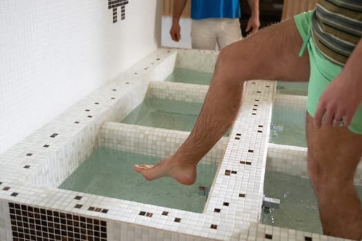 Close up of a mans legs as he steps into tiled spa therapy pools for a hydrotherapy session.