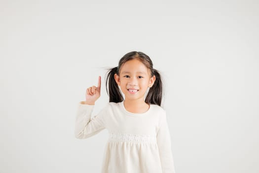 Asian happy portrait cute young kid girl makes gesture fingers point upwards above presenting product something, studio shot isolated on white background, kindergarten children woman smile
