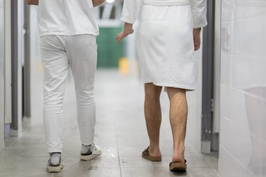 Medical Consultation in Spa Corridor.Two men discussing treatment options while walking through a clinical spa corridor, wearing white uniforms and bathrobe