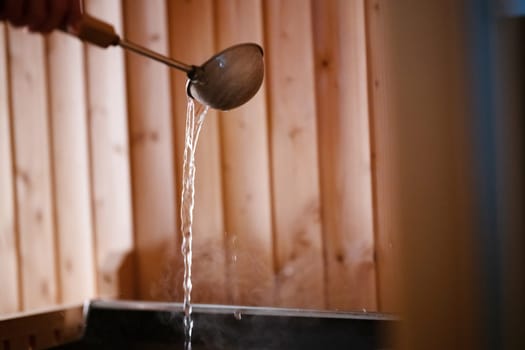 Detailed close up of sauna bucket with ladle and essential oils next to rolled towels on wooden bench inside sauna.