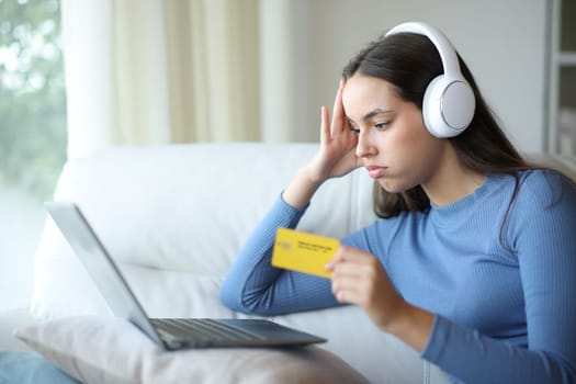 Frustrated woman wearing headphone buying entertainment content after mistake sitting on a couch at home