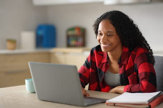 Happy black student e-learning using laptop in a kitchen at home