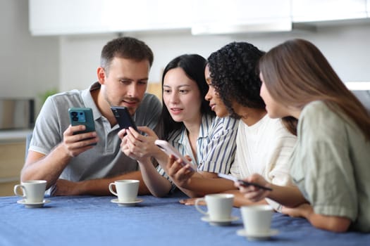 Four interracial friends checking their mobile phones in the kitchen at home