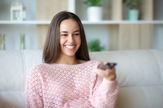 Happy woman using tv remote control sitting on a couch at home