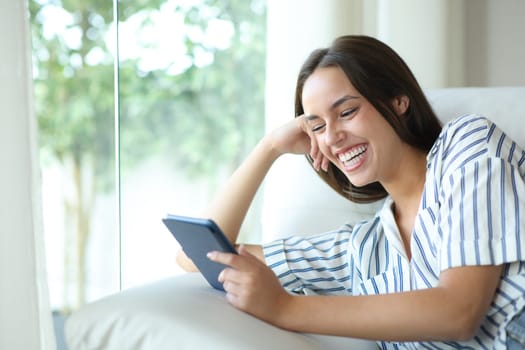 Happy woman reading ebook relaxing sitting on a couch at home