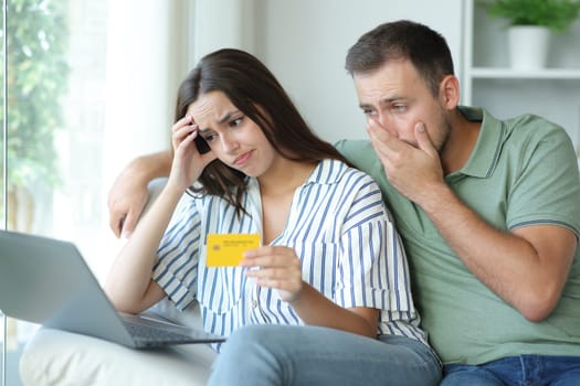 Worried couple having trouble paying online with credit card and laptop sitting on a couch at home