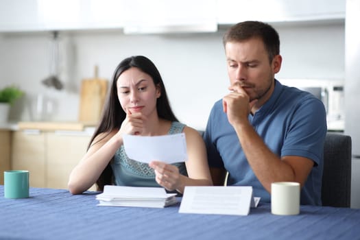 Suspicious interracial couple cheking bill in the kitchen at home