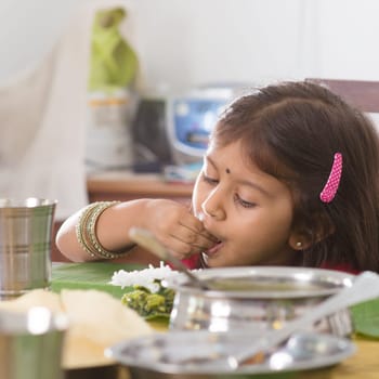 Indian family dining at home. Candid photo of Asian child self feeding rice with hand. India culture.