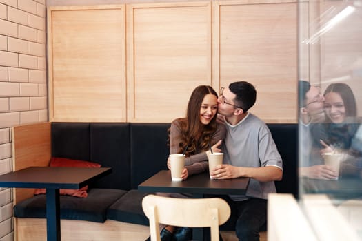 Two young individuals share a joyful moment in a modern cafe, sipping their drinks and smiling at each other. The inviting atmosphere enhances their connection.