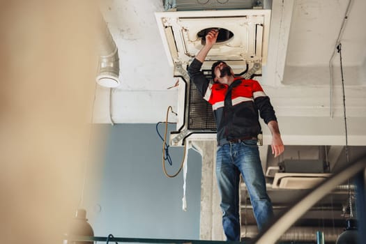 A construction worker is on a scaffold, inspecting and repairing the ceiling equipment in a newly designed office space filled with natural light. Black pendant lights hang overhead.