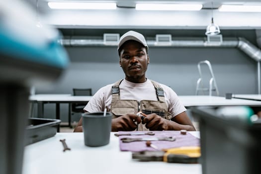 A technician is seated at a workstation in a contemporary workshop, meticulously assembling tools and parts, showcasing concentration and craftsmanship during daylight hours.