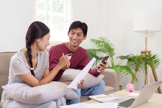 A young couple engages in a productive conversation about their finances, utilizing a smartphone and documents to plan their payments and budget effectively.