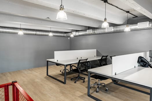 Spacious co-working area featuring sleek desks and ergonomic chairs, illuminated by industrial-style pendant lights. An ideal environment for collaboration and productivity during daylight hours.