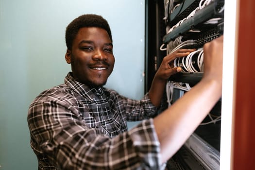 A technician smiles while managing network cables in a server room. The organized setup highlights his attention to detail in maintaining network infrastructure.