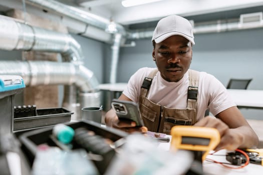 A technician is focused on handling tools while using a smartphone for assistance in a well-equipped workshop. The setting features modern design and metallic details.
