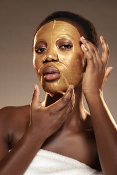 Soft, warm lighting highlights a woman in a towel. She delicately applies a gold facial mask, enhancing her skincare routine with a focus on relaxation and rejuvenation.