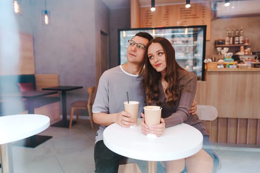 A couple sits closely at a small table in a cafe, sharing drinks and smiles. The cozy atmosphere and warm lighting create an inviting place for connection.