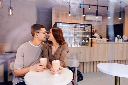 A couple sits closely at a small table in a cozy cafe, savoring their drinks and sharing smiles and laughter. The warm ambiance enhances their intimate connection.