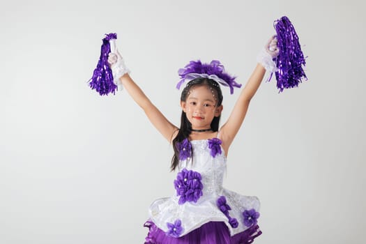 Smiling kid cheerleader in purple and white uniform, holding pom-poms. Studio shot with a clean white background. Youthful energy and celebration. cheerleader kid