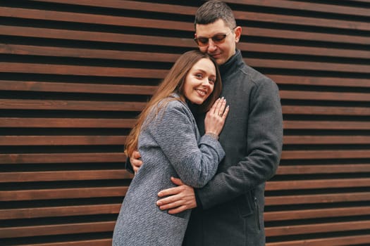 A couple enjoys a moment together, embracing warmly while standing in front of a wooden slatted wall.