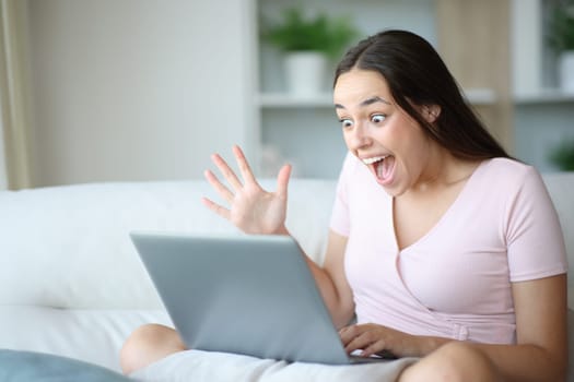 Amazed woman watching astonishing content on laptop sitting at home