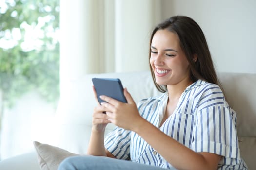 Happy woman reading ebook sitting on a couch at home