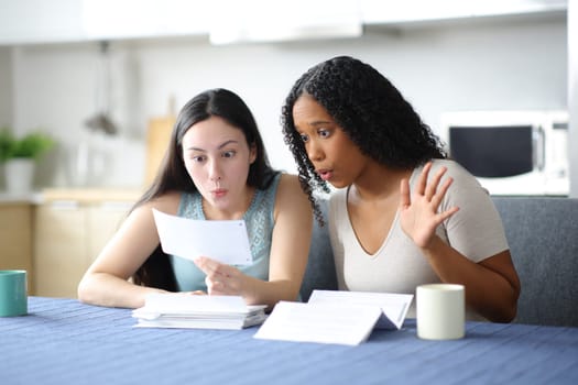 Surprised interracial women checking bank statement in the kitchen at home