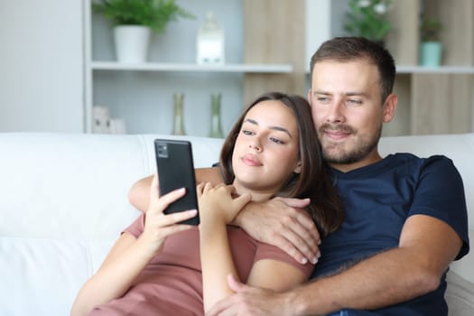 Serious couple checking phone together sitting on a couch at home