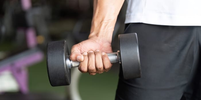 A muscular man grips a dumbbell, showcasing strength training and dedication to fitness in a gym environment.