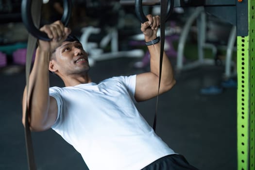 A young man performs a pull-up exercise on gym rings, showcasing his strength and dedication to fitness in a modern gym setting.