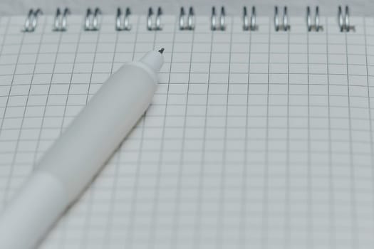 Close-up of white pen tip on grid notebook page. Concept of writing, note-taking, planning, education, stationery, and creative workspace.