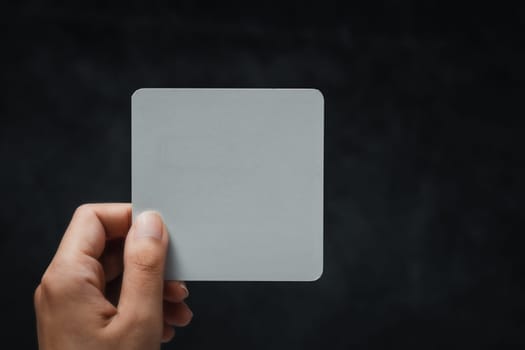 Woman's hand holding white note against black background. Concept of message, communication, minimal design, announcement, and copy space for text or branding.