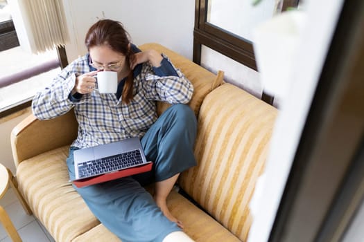 Freelancer enjoying a cup of coffee while working remotely from her comfortable sofa