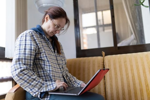 Woman sitting on couch using laptop, working remotely from home office