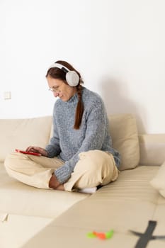 Woman enjoying music with headphones and browsing her smartphone while relaxing on a comfortable sofa in her living room