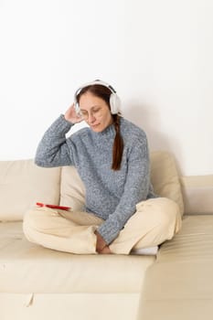 Woman wearing headphones enjoying music on her smartphone while relaxing on a comfortable sofa
