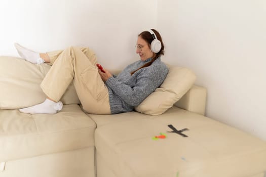 Mature woman enjoying music with headphones while using smartphone on a comfortable sofa at home