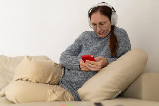 Woman wearing headphones and using smartphone while relaxing on a comfortable sofa at home