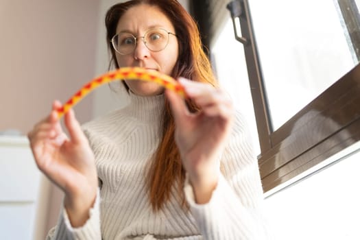 Woman wearing glasses and a white sweater holding a bent candy and looking surprised