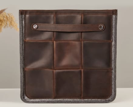 Brown leather organizer bag with small handle and gray felt edges standing on a neutral background