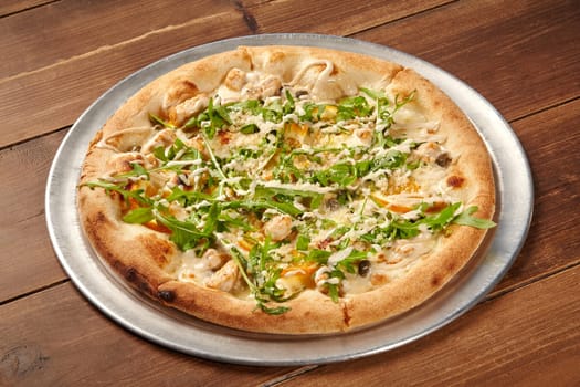 Tasty pizza featuring grilled chicken, fresh arugula, and parmesan cheese, served on a wooden table