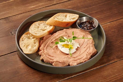 Creamy chicken liver pate served with quail egg, onion marmalade and toasted bread on a wooden table