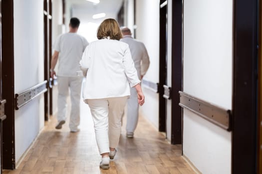 A group of healthcare professionals in white uniforms walking through a hospital hallway while reviewing patient documents and discussing treatment plans