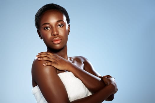 A woman with short dark hair poses confidently against a pale blue backdrop, her arms crossed, exuding grace and self-assurance. The soft lighting highlights her radiant skin.