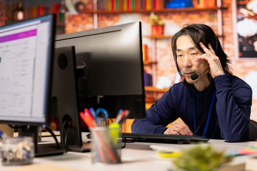 Call center agent speaking in audio headset microphone, using remote access tools. Worker in customer center assisting clients with installing software, communicating through headphones mic