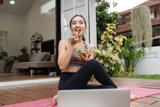 A woman enjoying a fresh salad after a yoga session, embodying a lifestyle of health and mindfulness in her home.