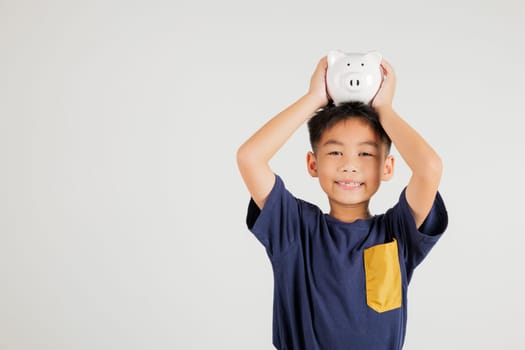 Asian little kid boy holding piggy bank bank over head in studio shot isolated on white background, Happy primary child lifestyle smiling with is white piggybank, Thai personal money savings