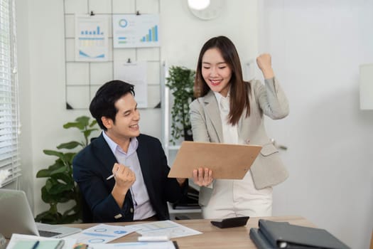 Two colleagues excitedly discuss financial achievements and strategies in a bright office, showcasing teamwork and collaboration.