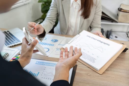 In a professional setting, two business experts discuss financial charts and use a calculator to strategize financial decisions.