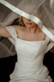 Close-up, blurry shot of bride putting on veil. sharpness on veil. Beautiful bride Fashion portrait in wedding luxury dress with lace and crystals in dark interior.